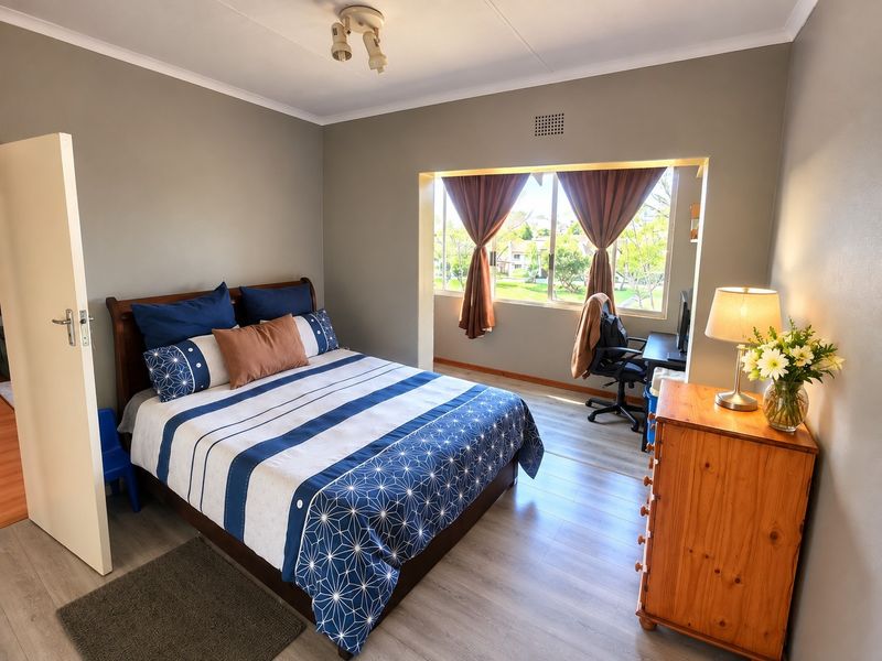 A well-lit bedroom featuring laminate flooring, a large window with natural light, and a neutral wall finish.