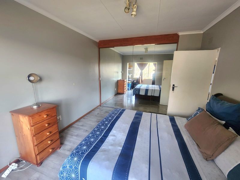 A bedroom featuring laminate flooring and a large built-in mirrored wardrobe, offering ample storage space and a bright, functional layout.