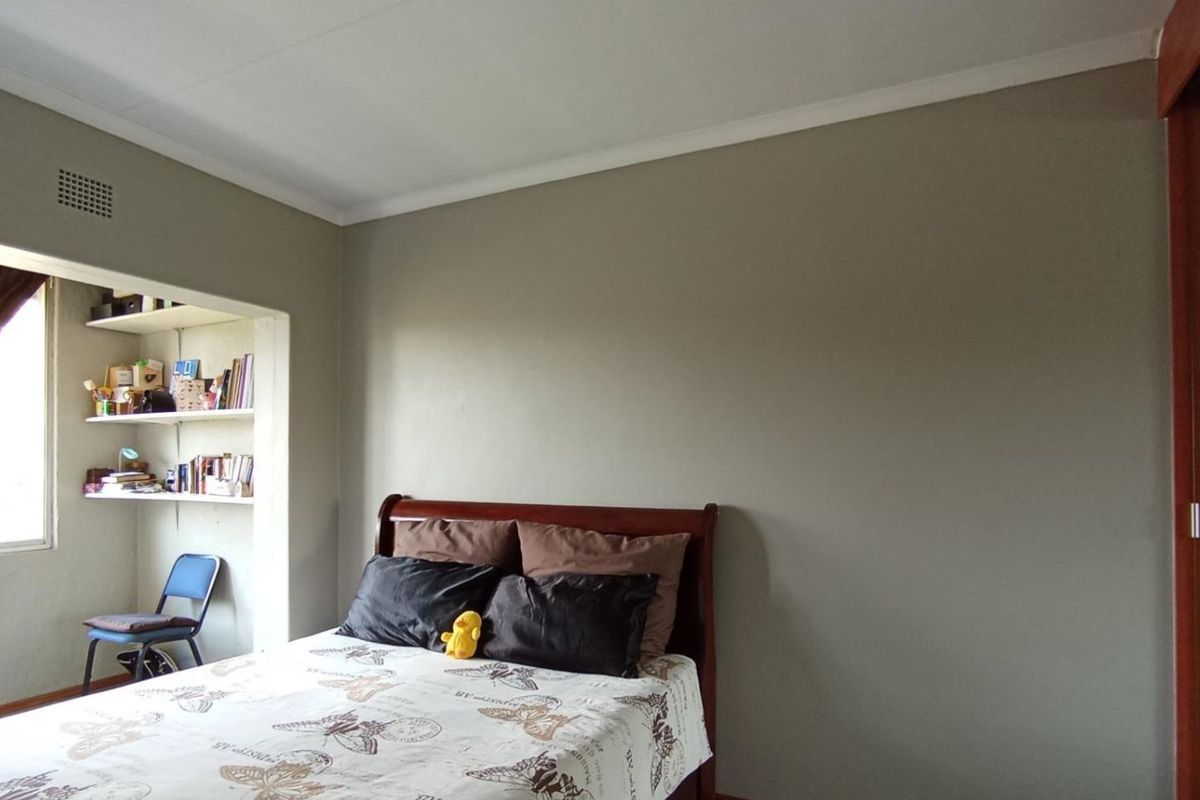 A bedroom featuring neutral wall tones, built-in shelving in a recessed alcove, and a sliding door, offering a functional and well-lit living space.