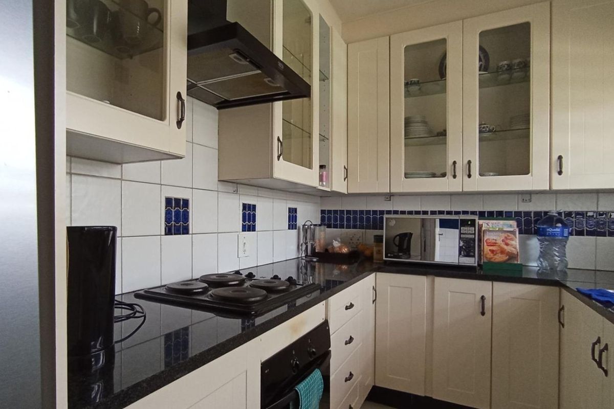 A functional kitchen featuring cream cabinetry, dark granite countertops, a tiled backsplash with decorative accents, and integrated cooking appliances.