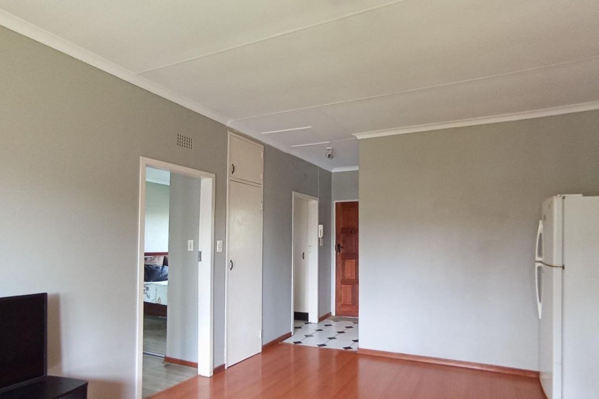 A neutral living area featuring laminate flooring, built-in storage cupboards, and access to adjacent rooms via a central hallway.
