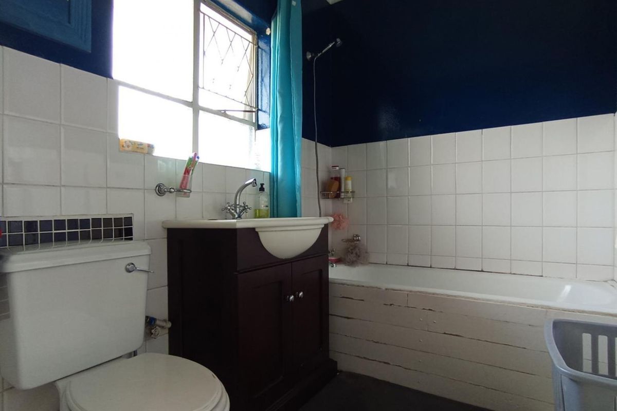 A functional bathroom featuring a bathtub, vanity basin, and toilet, with tiled walls and a window for natural light.