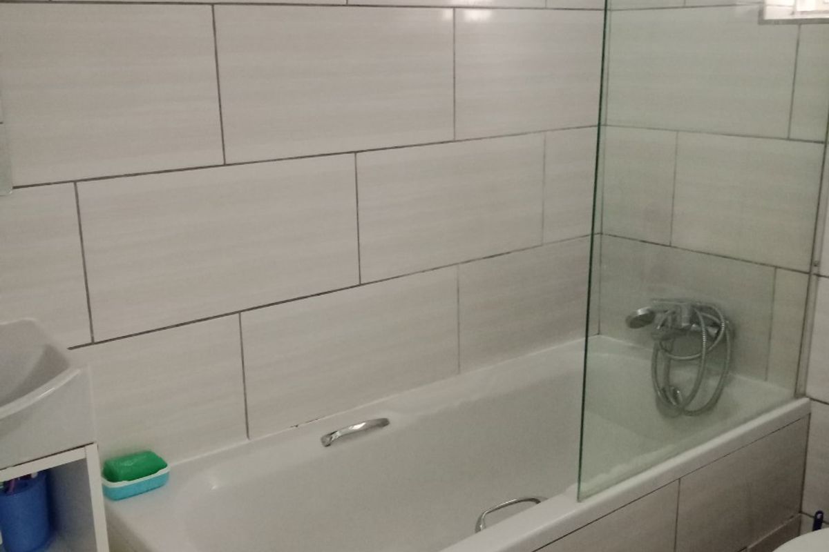 A modern bathroom featuring a bathtub with a glass shower screen, wall-to-wall tiling, and a standard toilet.