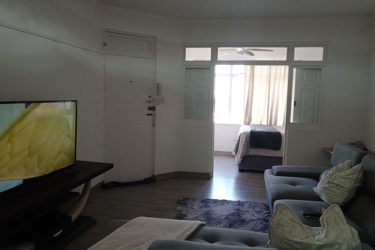 A living room area featuring laminate flooring and an internal glass-paneled door leading to an adjacent bedroom space.