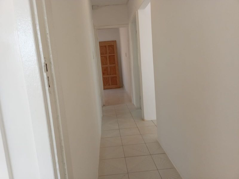 A simple, empty hallway featuring tiled flooring and multiple internal doorways, providing access to various rooms within the property.