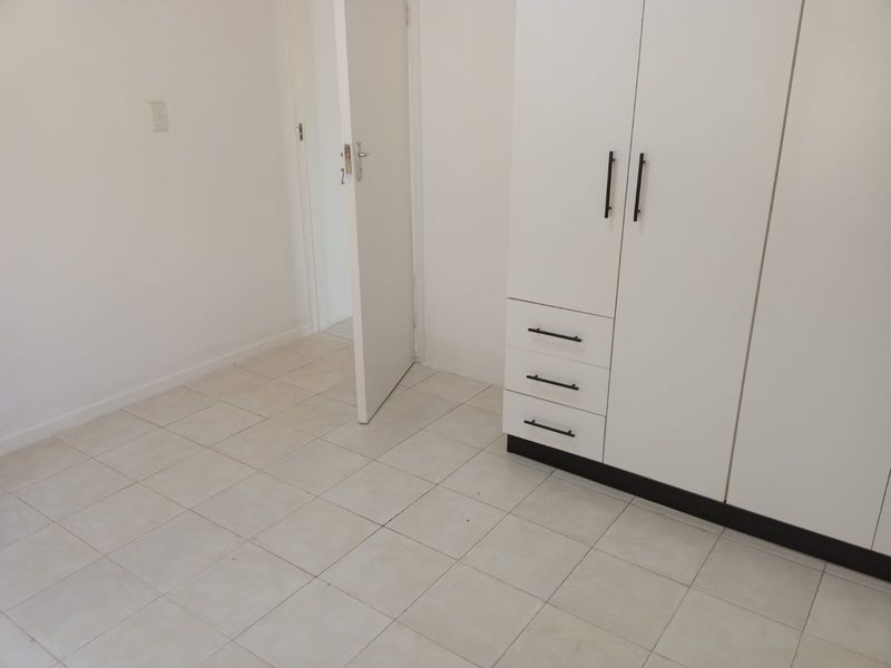 A clean, empty bedroom featuring neutral tiled flooring and a modern white built-in wardrobe with black hardware.
