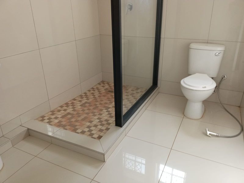A clean, modern bathroom featuring a walk-in shower with a glass screen, neutral wall tiles, and a standard toilet.