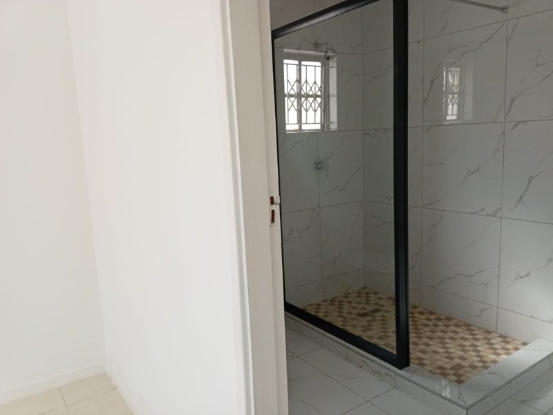 A modern bathroom featuring a walk-in shower with a black-framed glass screen, marble-look wall tiling, and mosaic floor accents.