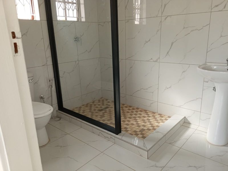 A modern bathroom featuring a walk-in shower with a black-framed glass screen, pedestal basin, and marble-look wall tiling.