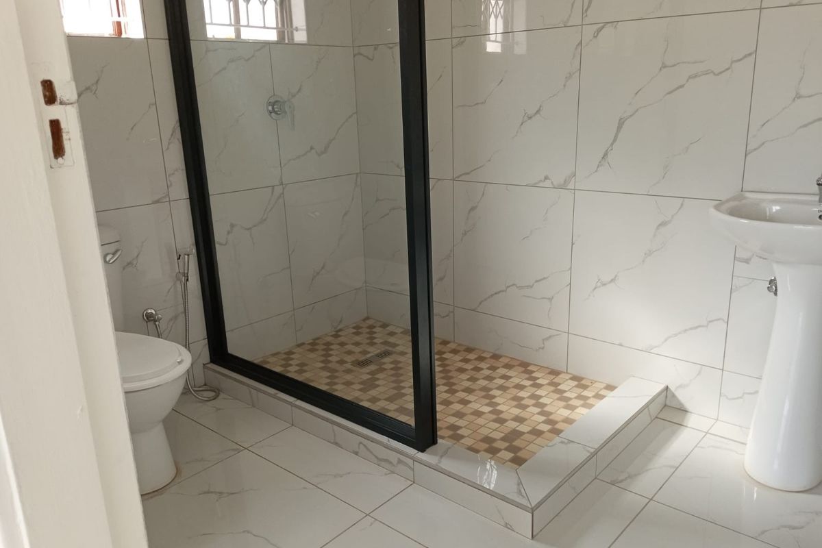 A modern bathroom featuring a walk-in shower with a black-framed glass screen, pedestal basin, and marble-look wall tiling.