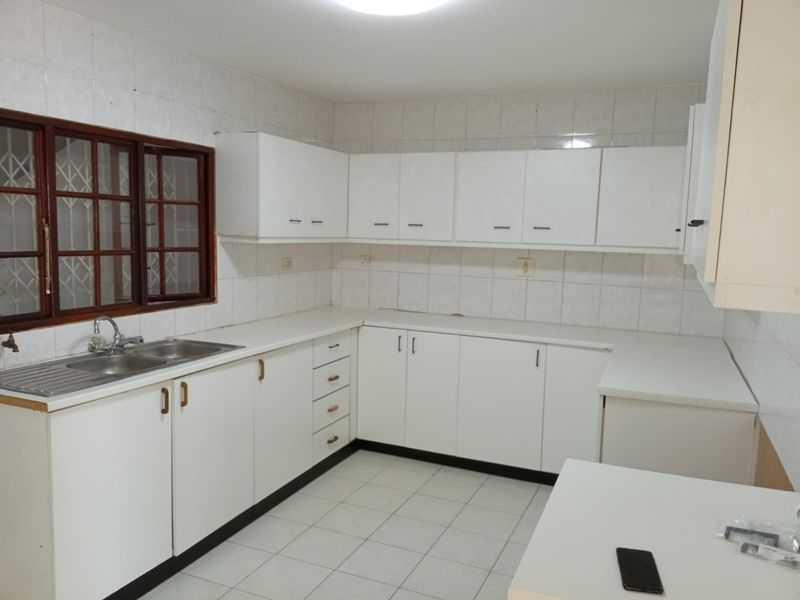 A functional kitchen featuring white built-in cabinetry, a double bowl stainless steel sink, tiled backsplash, and tiled flooring.