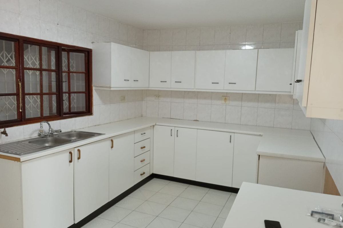 A functional kitchen featuring white built-in cabinetry, a double bowl stainless steel sink, tiled backsplash, and tiled flooring.