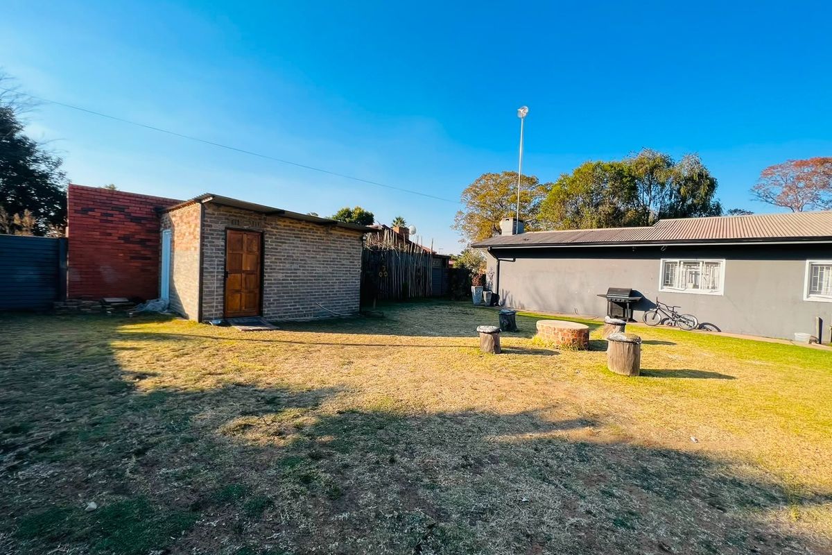 A spacious rear garden area featuring a detached brick outbuilding, a main house structure, and a lawned yard.