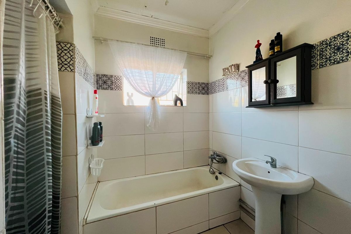 A functional bathroom featuring a tiled bathtub surround, pedestal basin, and decorative wall tiling.