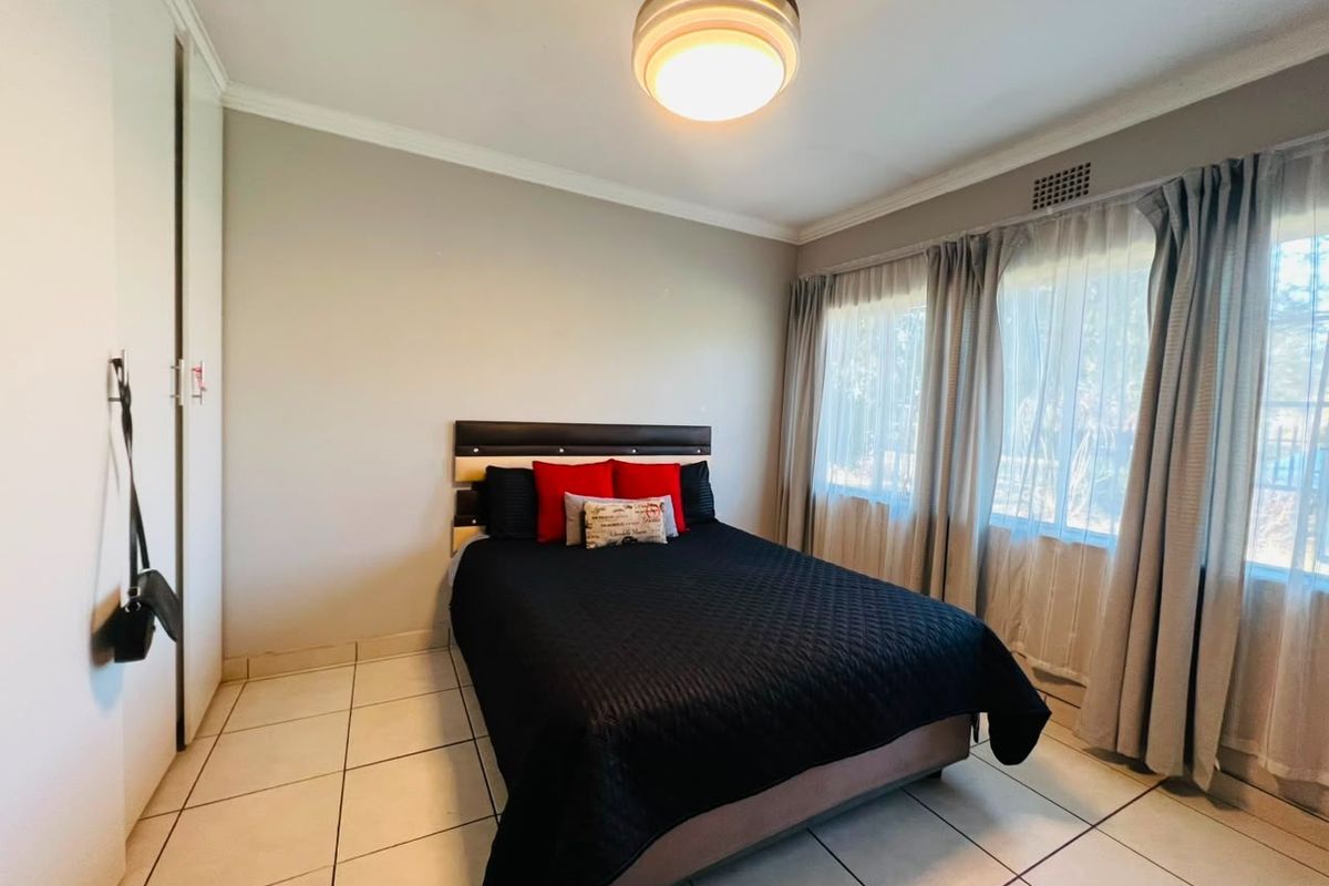 A well-lit bedroom featuring tiled flooring, built-in cupboards, and large windows with curtain tracks, offering a functional and comfortable living space.