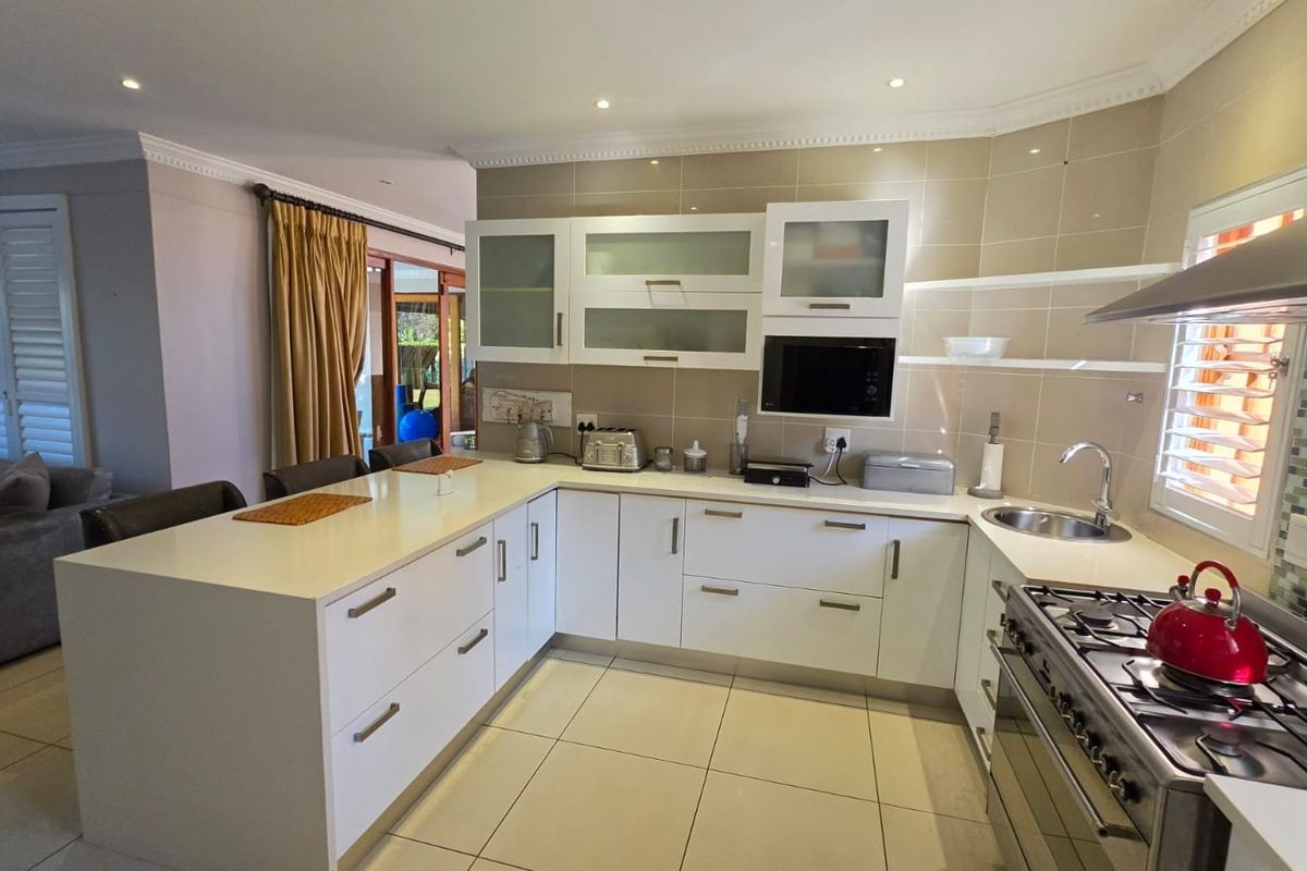 Modern kitchen featuring white cabinetry, gas cooktop, stainless steel extractor fan, tiled splashback, and a breakfast bar island, seamlessly integrated into an open-plan living space.