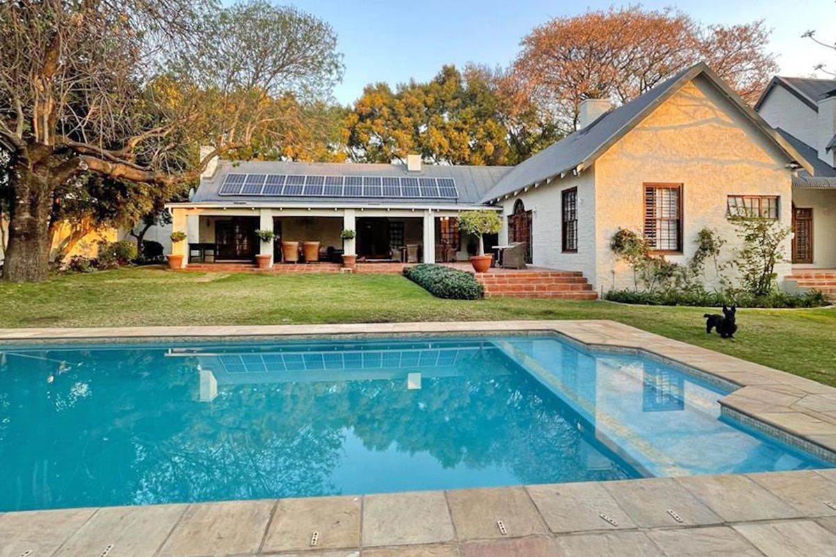 Rear view of the house featuring a swimming pool, covered patio area, and roof-mounted solar panels set within a landscaped garden.