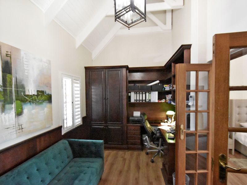 A well-appointed home office featuring custom built-in cabinetry, a dedicated desk area, vaulted ceilings, and elegant timber shutters.