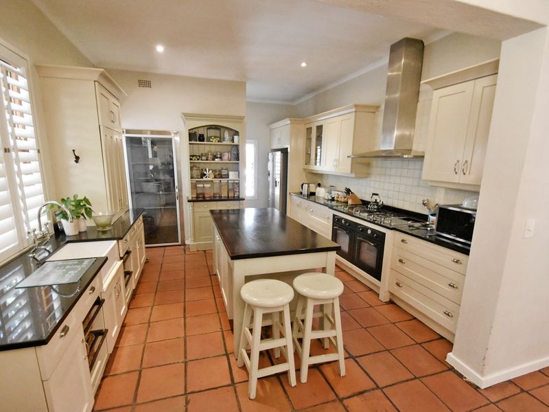 Spacious kitchen featuring a central island, farmhouse sink, granite countertops, built-in cabinetry, and high-quality stainless steel appliances with classic terracotta flooring.