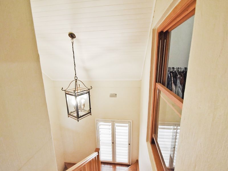 A bright, elevated view of a hallway featuring a timber staircase, vaulted ceiling, and a classic pendant light fixture.
