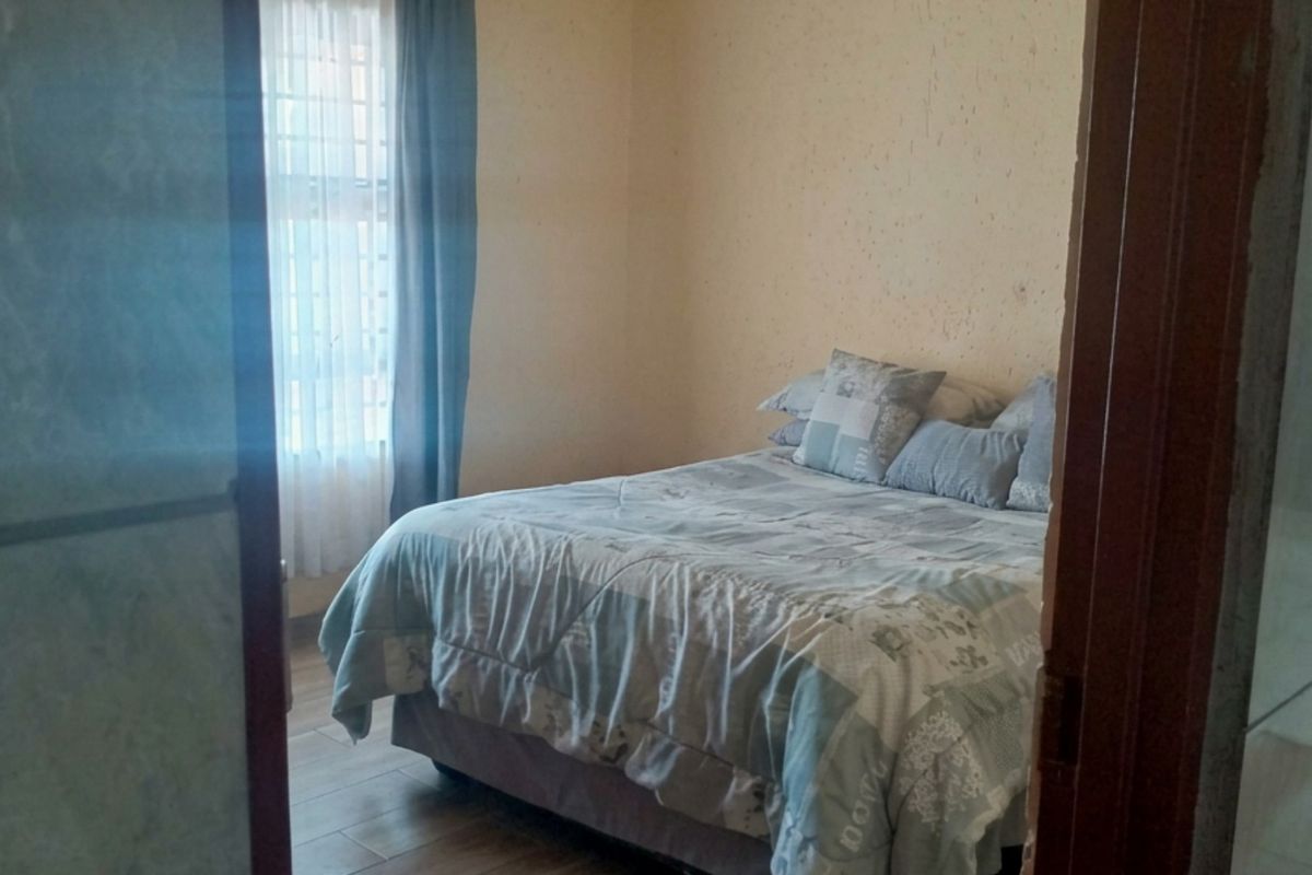 A bedroom featuring tiled flooring and a window with curtains, showing signs of wear on the wall surfaces.