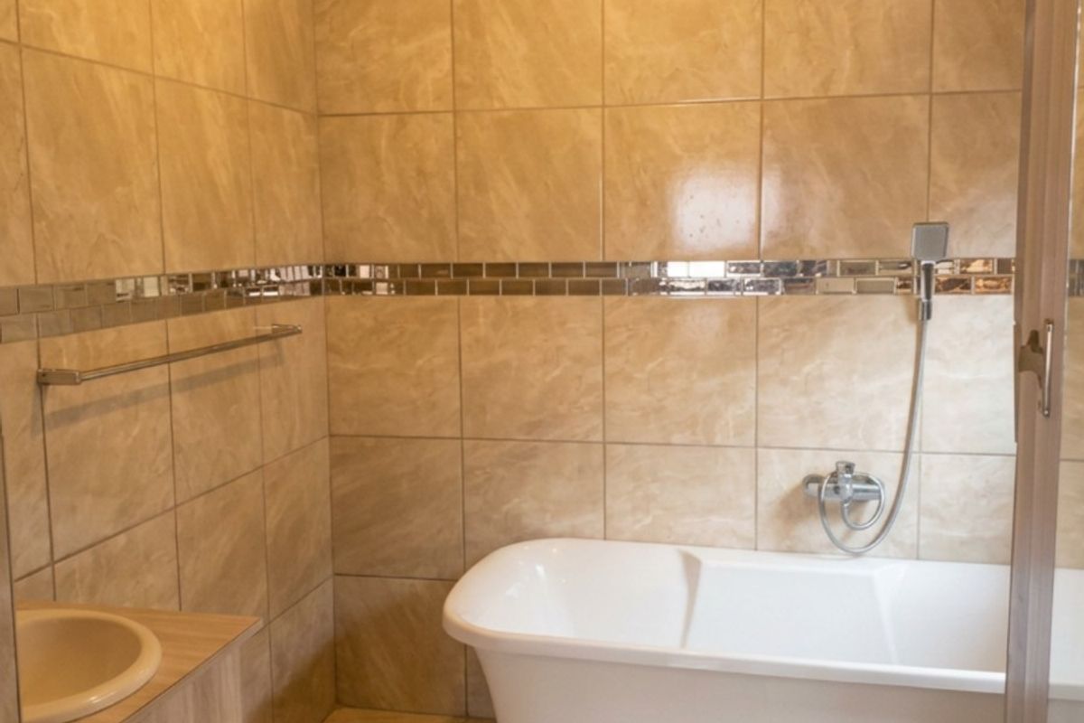 A modern bathroom featuring floor-to-ceiling beige tiles, a freestanding bathtub with handheld shower fixture, and a built-in vanity unit.