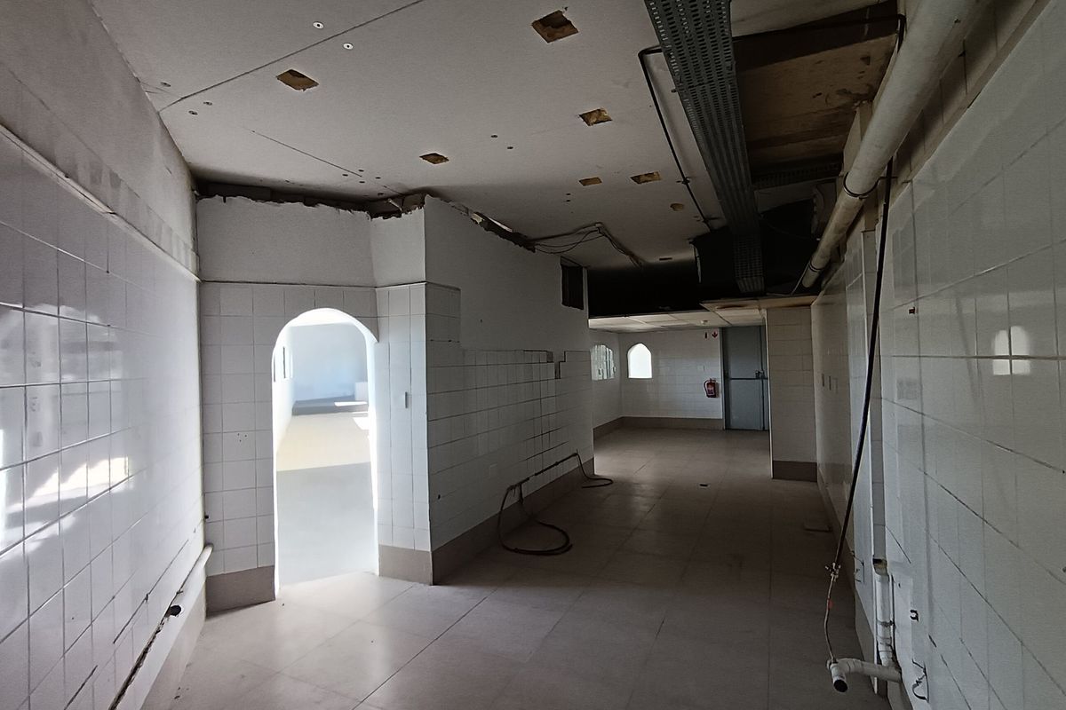 An unfinished commercial kitchen space featuring tiled walls, exposed ceiling infrastructure, and an arched doorway, currently in need of significant renovation and completion.