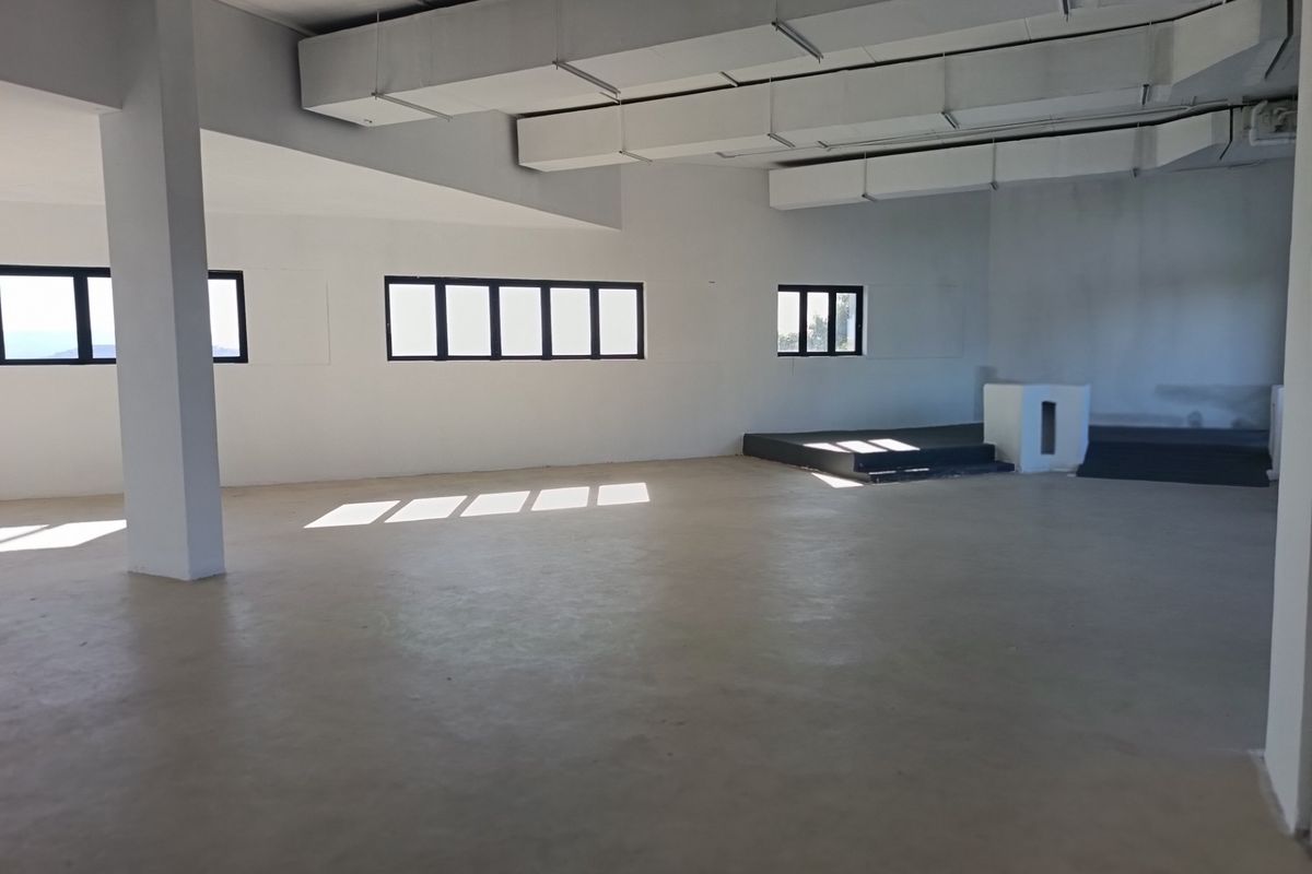 A spacious, open-plan restaurant interior featuring exposed ceiling ductwork, concrete flooring, and a raised platform area, offering a blank canvas for custom fit-out.