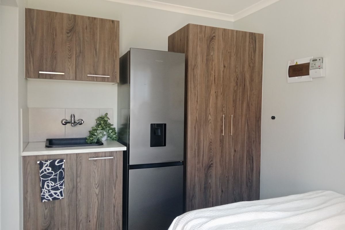 A compact kitchenette featuring wood-grain cabinetry, a modern sink, and integrated storage, providing functional utility within a bedroom or studio space.
