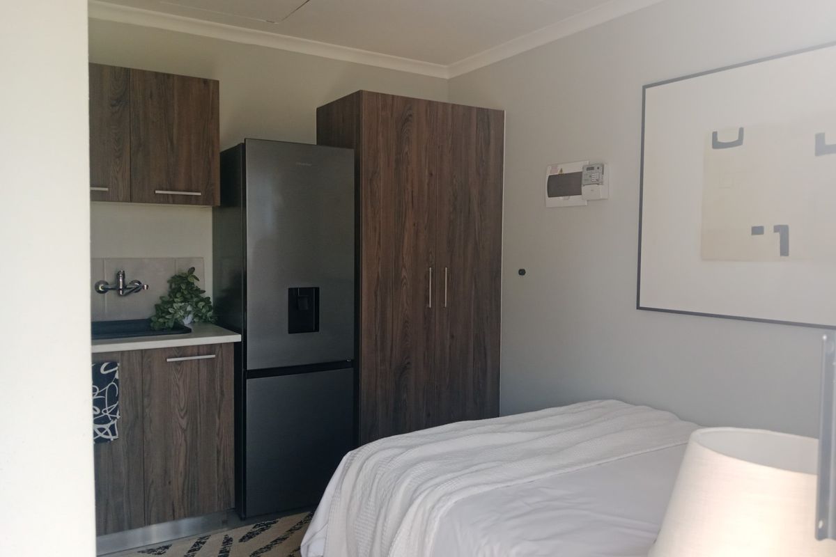 A compact bedroom featuring a built-in wardrobe and a convenient kitchenette area with cabinetry and sink, ideal for studio-style living.