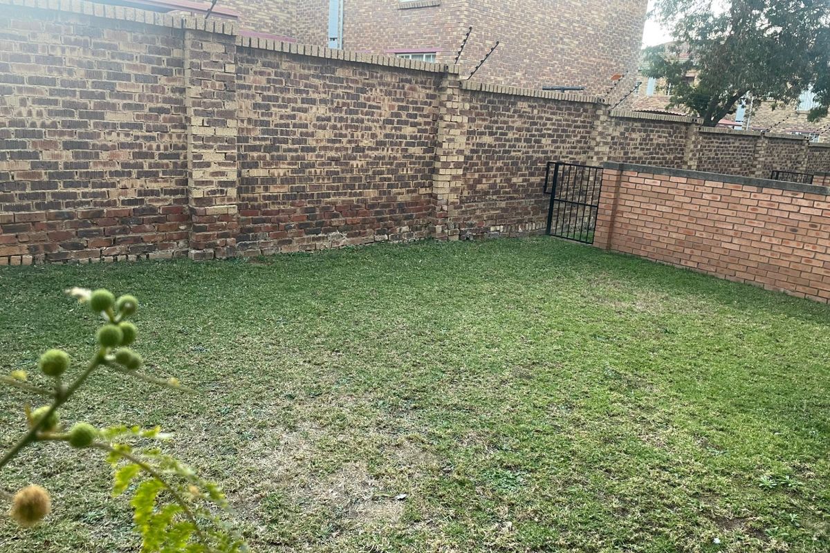 A private rear garden area enclosed by high brick boundary walls with integrated electric fencing and a secure metal pedestrian gate.
