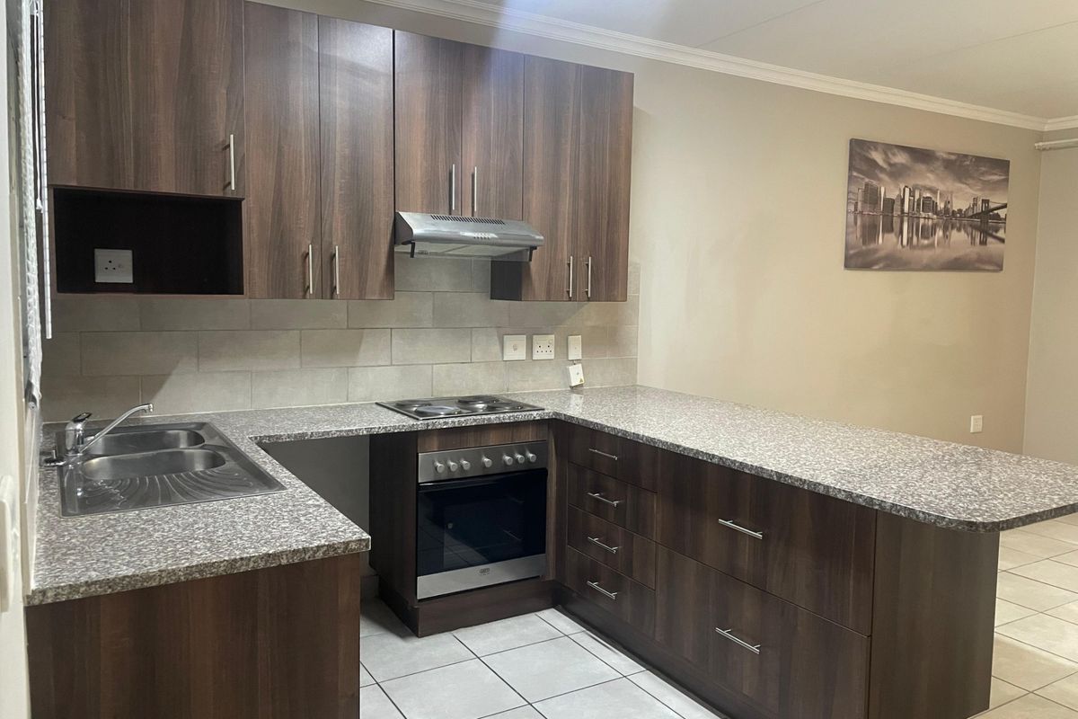 Modern kitchen featuring dark wood cabinetry, granite countertops, built-in oven, electric hob, extractor fan, and tiled flooring.