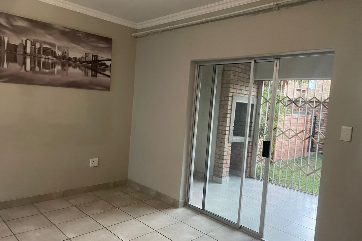 An empty living room featuring neutral tiled flooring, crown molding, and a sliding glass door providing access to an outdoor patio area.