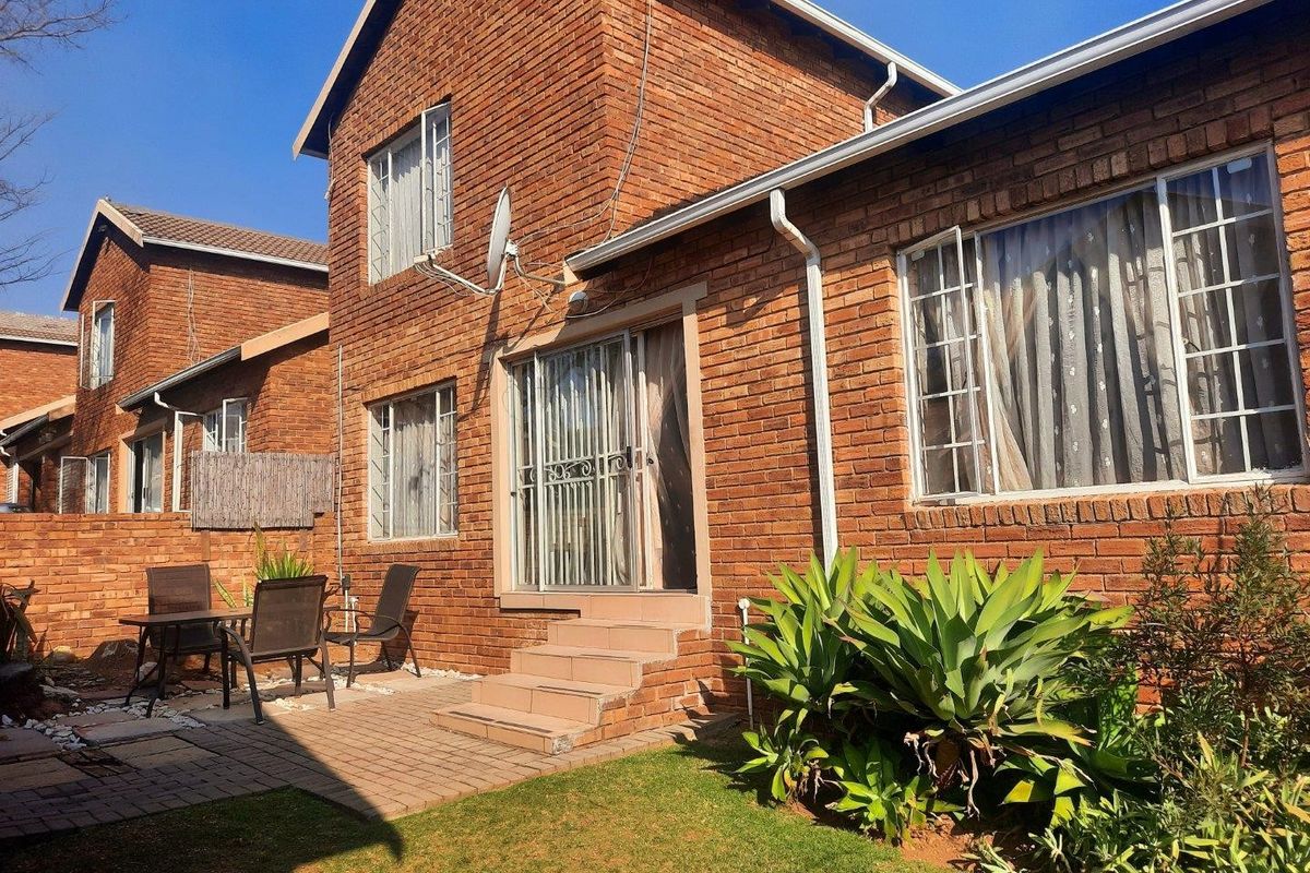 Rear view of a double-story face brick townhouse featuring a paved patio area, sliding door access, and established garden landscaping.