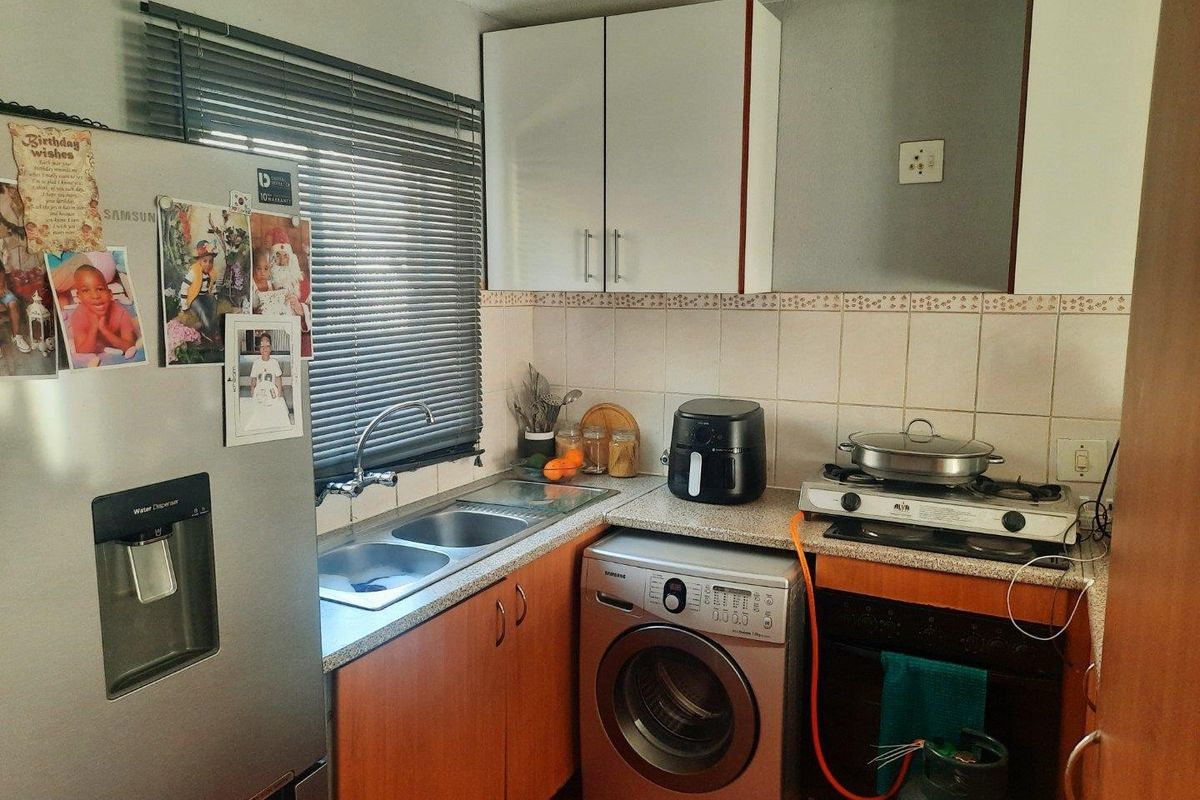Compact kitchen featuring built-in cabinetry, double sink, gas hob, and oven with tiled backsplash and venetian blinds.