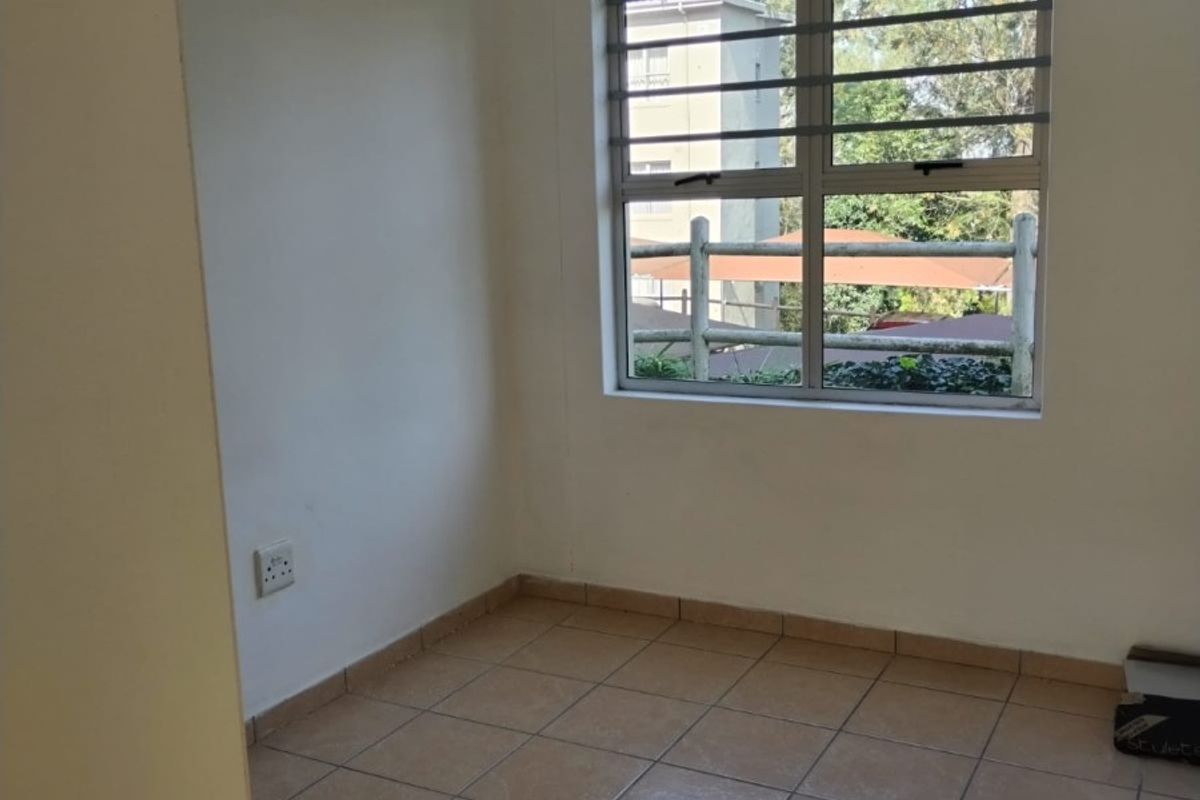 A bright, empty bedroom featuring neutral tiled flooring and a window fitted with security bars, offering a clean and versatile living space.