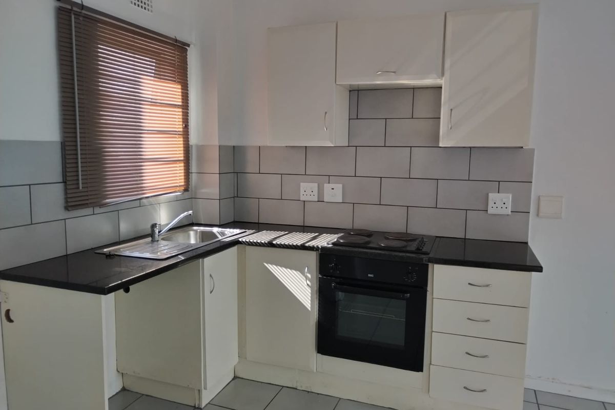 A functional kitchen featuring white cabinetry, dark countertops, subway tile backsplash, and built-in oven with electric hob.