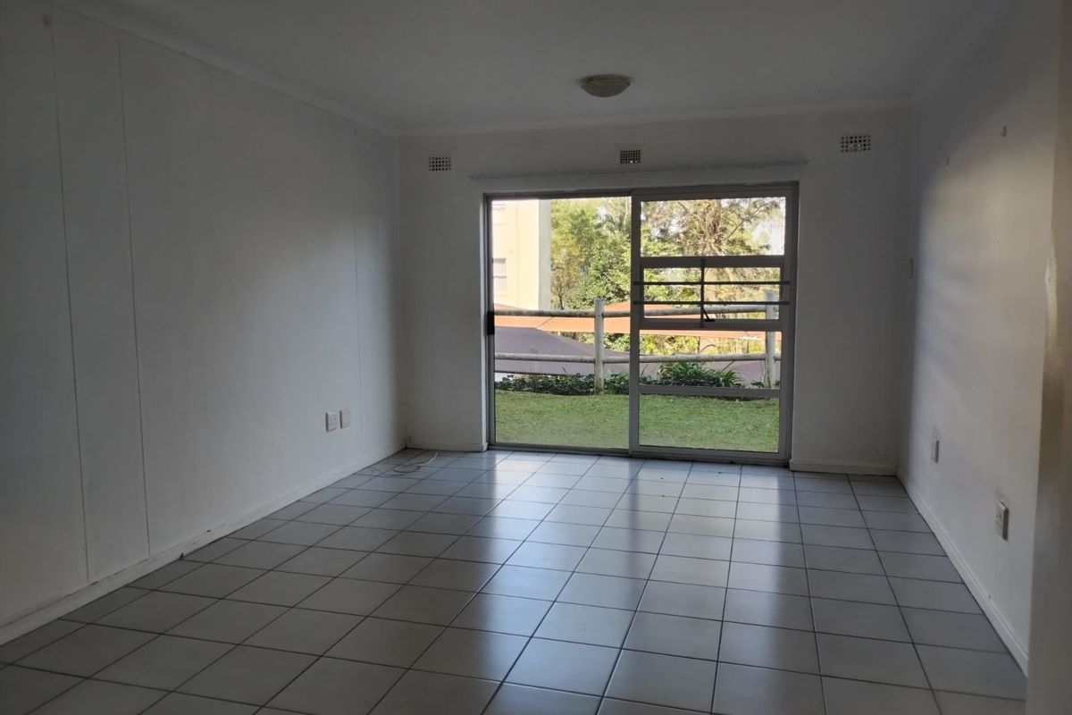 An empty living room featuring ceramic floor tiles and a large sliding glass door providing natural light and access to the exterior.