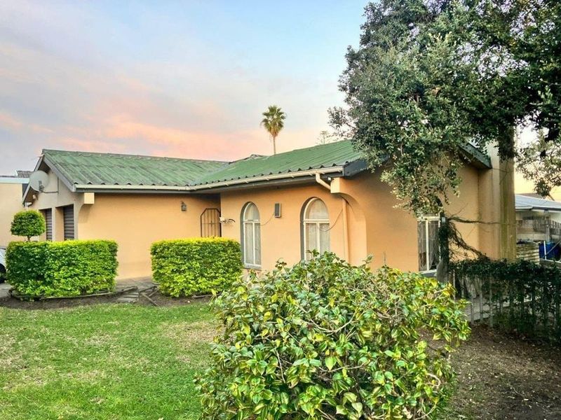 Rear view of a single-story house featuring a pitched metal roof, arched windows, and a surrounding garden area.