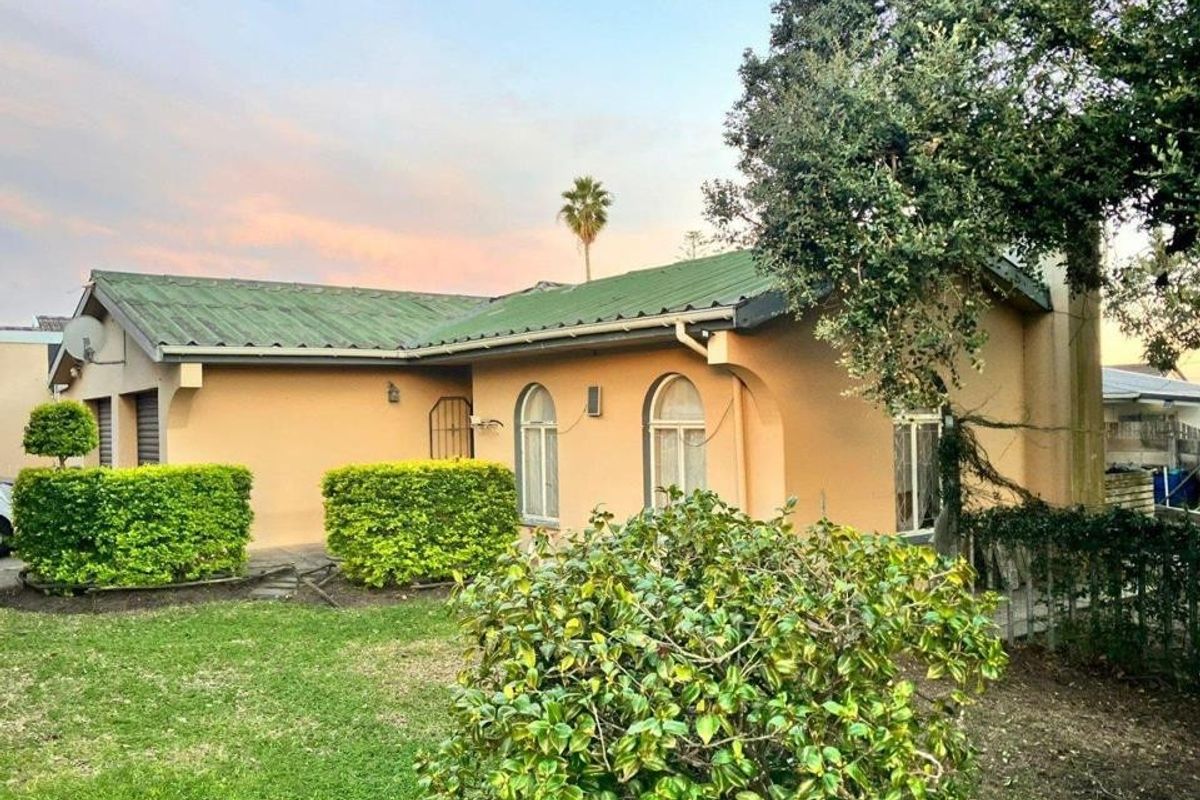 Rear view of a single-story house featuring a pitched metal roof, arched windows, and a surrounding garden area.