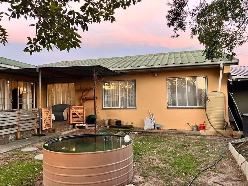 Rear view of the property featuring a corrugated metal roof, exterior wall finish, and a garden area with a water tank.