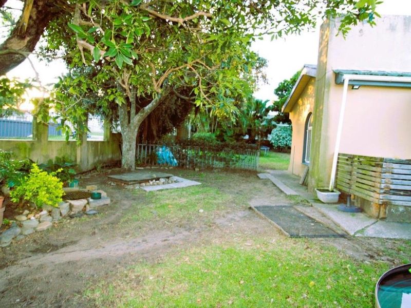 Rear garden area featuring a lawn, mature tree, perimeter wall, and concrete patio space adjacent to the house exterior.