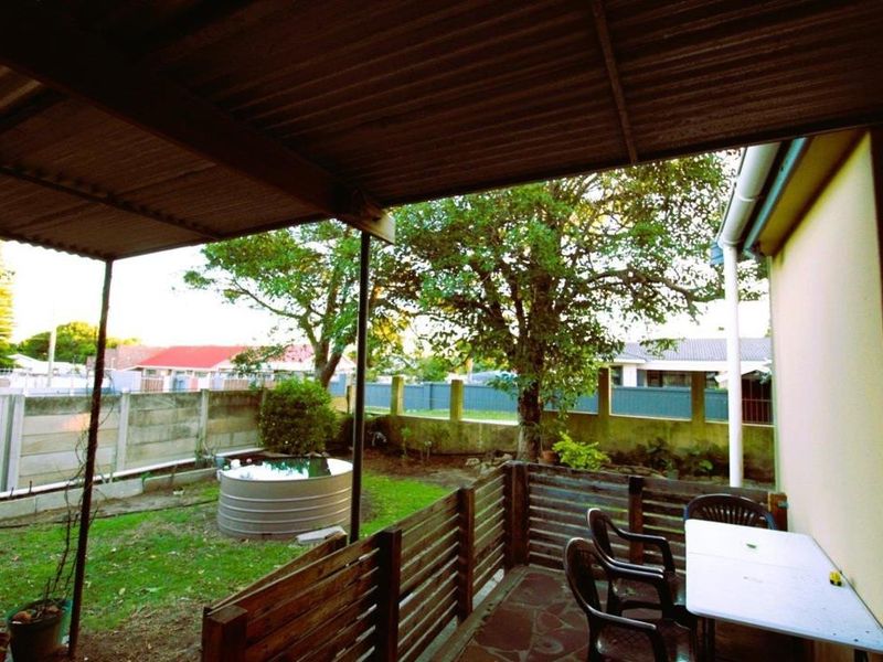 A covered patio area featuring stone paving and timber fencing, overlooking a private garden with a rainwater tank and boundary wall.