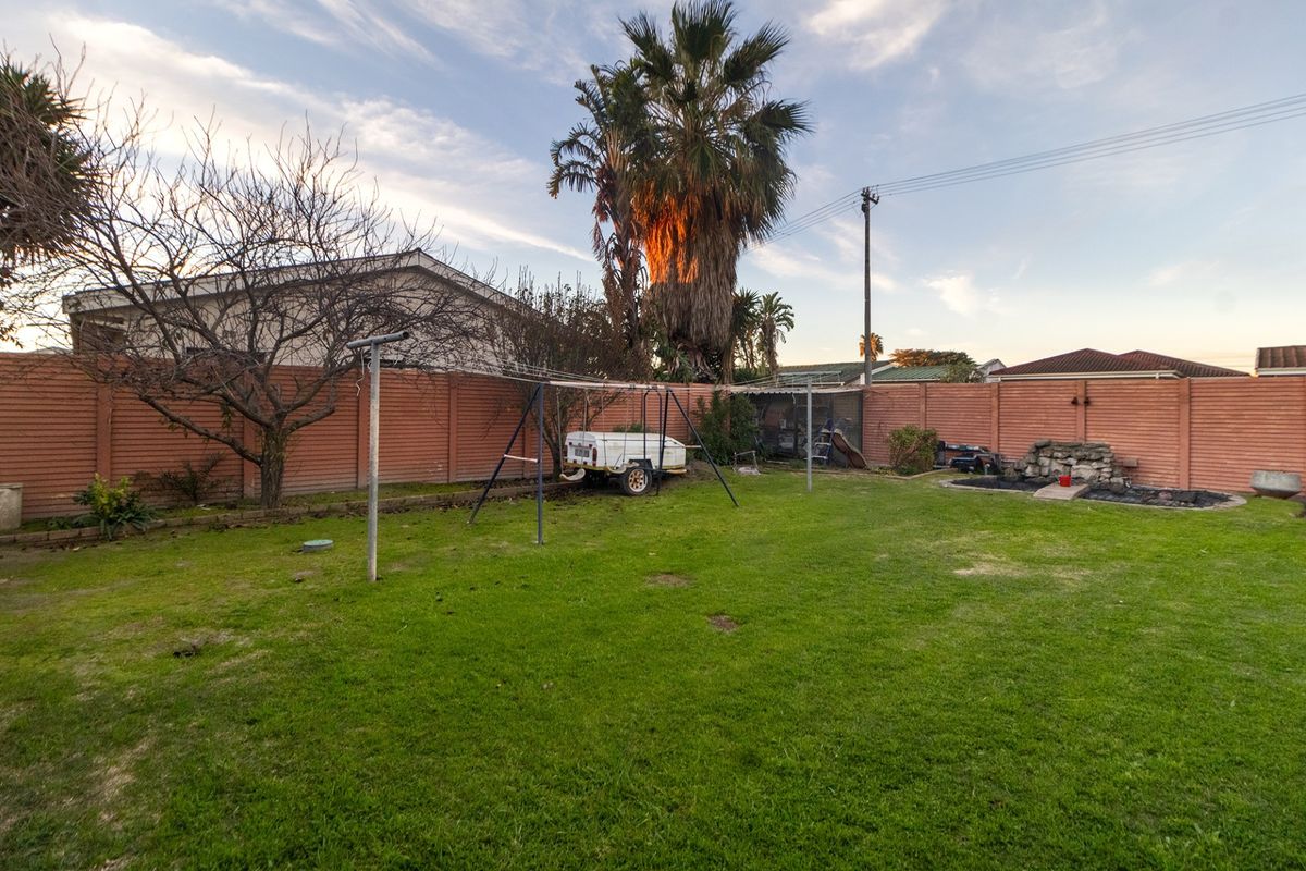 A spacious rear garden featuring a lawn, perimeter precast concrete walling, a fixed washing line, and a stone water feature.