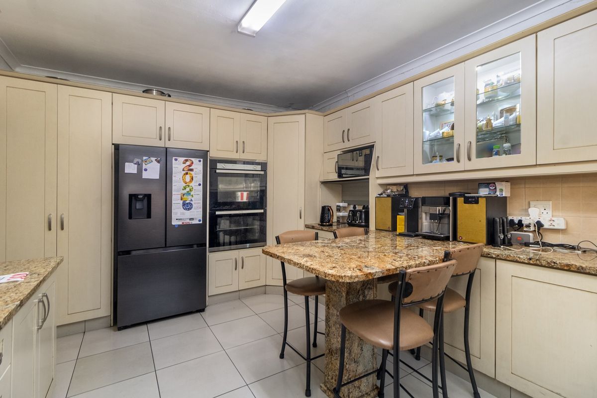 A functional kitchen featuring cream cabinetry, granite countertops, a double wall oven, and tiled flooring with a central breakfast bar area.