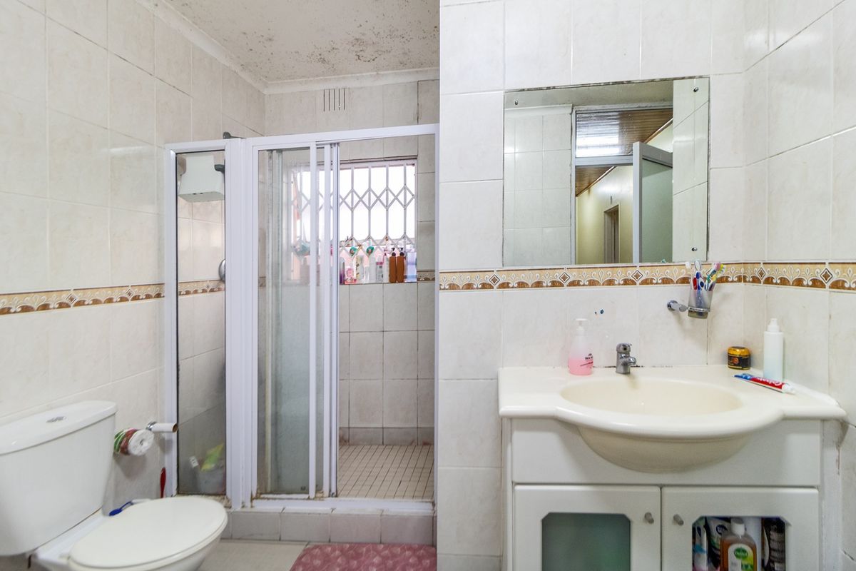 A functional bathroom featuring a shower enclosure, vanity cabinet with basin, and wall-mounted mirror, requiring cosmetic updates to address ceiling staining and dated finishes.