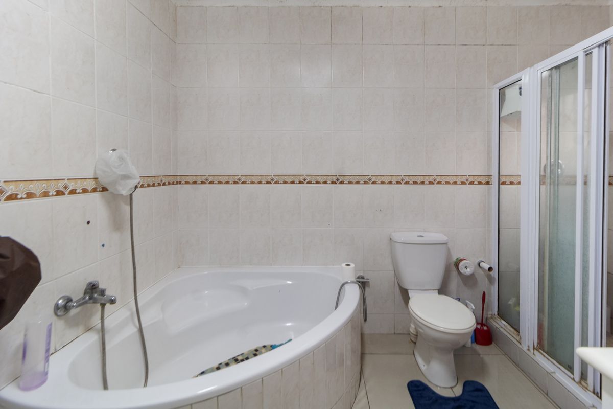 A functional bathroom featuring a corner bathtub, a separate shower enclosure, and a standard toilet with tiled walls and flooring.