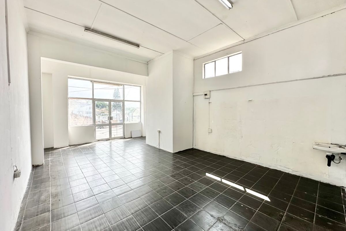 An empty commercial office space featuring dark tiled flooring, large storefront windows, and a wall-mounted basin, suitable for retail or professional use.