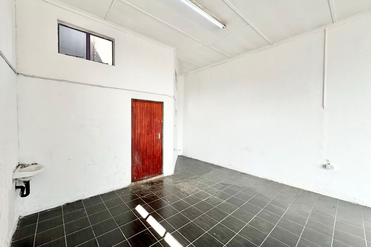 A vacant utility space featuring dark ceramic floor tiles, a wall-mounted basin, and a timber door, suitable for storage or a functional work area.