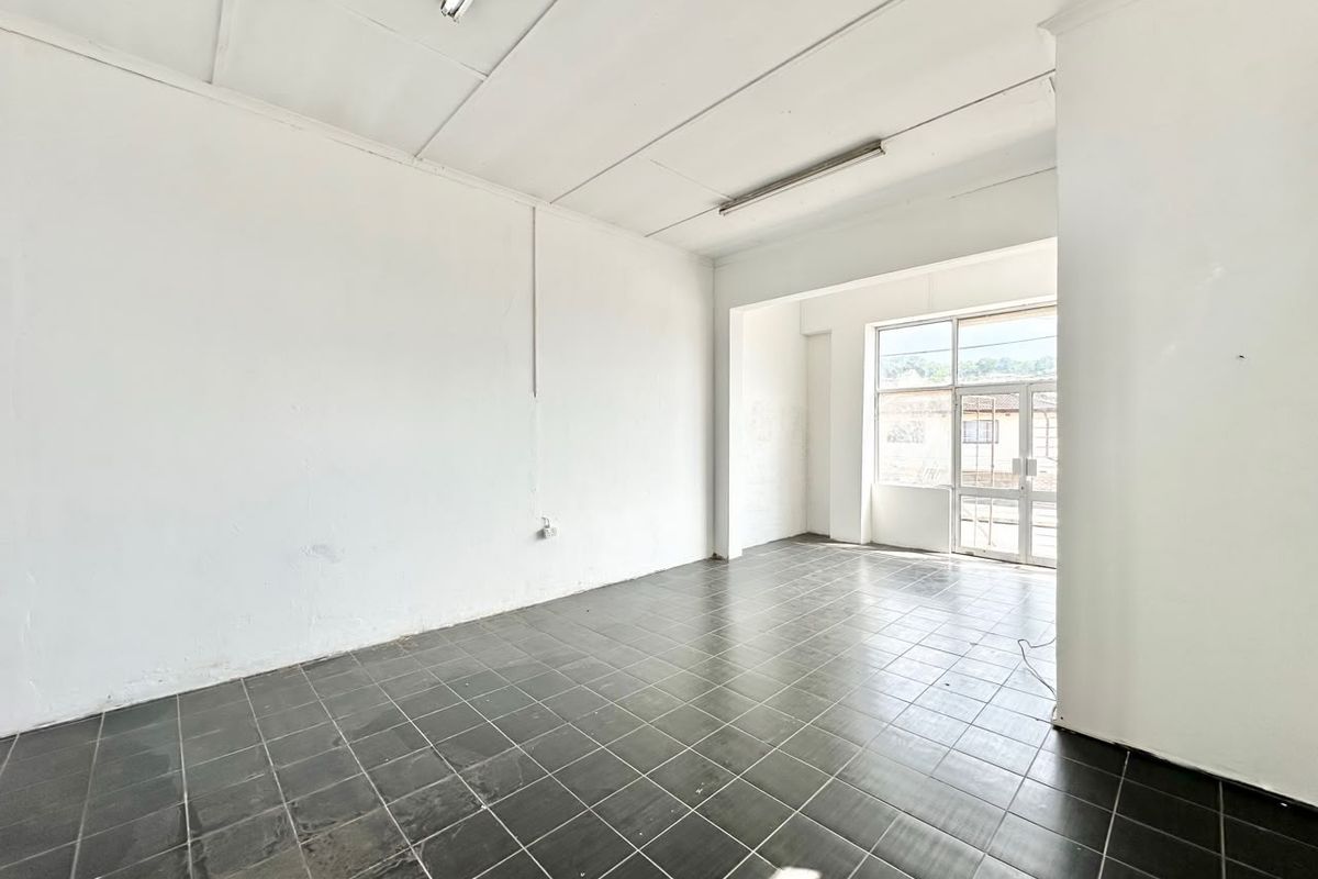 An empty commercial office space featuring tiled flooring, fluorescent lighting, and a glass entrance door, offering a blank canvas for business customization.